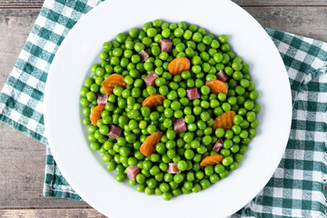 Green peas with serrano ham and carrot on wooden table