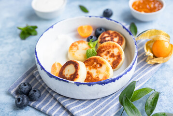 Cheese pancakes, fritters or syrniki with blueberry, physalis and yogurt, blue background. Healthy and tasty breakfast.
