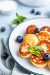 Cheese pancakes, fritters or syrniki with blueberry, physalis and yogurt, blue background. Healthy and tasty breakfast.