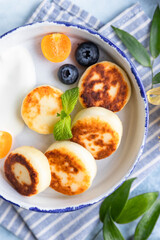 Cheese pancakes, fritters or syrniki with blueberry, physalis and yogurt, blue background. Healthy and tasty breakfast.