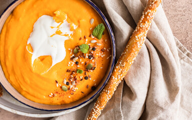 Pumpkin and carrot soup with cream, mint and seeds, brown concrete background. Traditional autumn or winter vegetarian soup with a creamy silky texture.