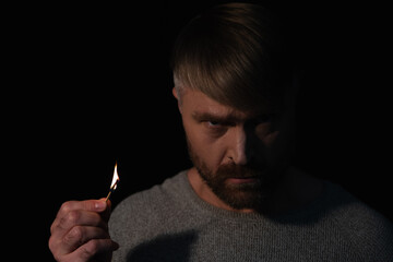 angry man holding lit match and looking at camera during power blackout isolated on black.