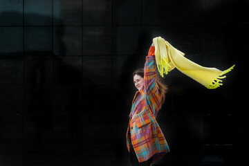 Young woman with yellow scarf in the windy in winter city. Black background. Contrasted colours. High quality photo