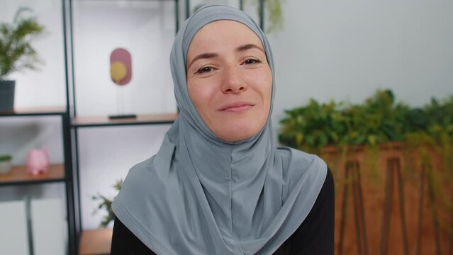 Portrait of happy calm young muslim business woman wearing hijab headscarf smiling friendly, glad expression, taking off glasses relaxation feel satisfied concept good news. Girl at modern home office