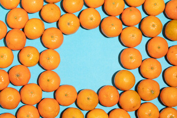 Irregular juicy tangerines, jumbled, on a blue background, with copy space in the centre empty, forming a pop art style image