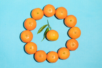Irregular juicy tangerines on a blue background, forming a circle with a different one in the middle, with leaves, in a pop art style