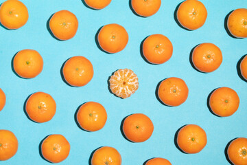 Juicy and healthy tangerines, one of them peeled, irregular shapes, arranged on a blue background, forming a pop art style image and texture