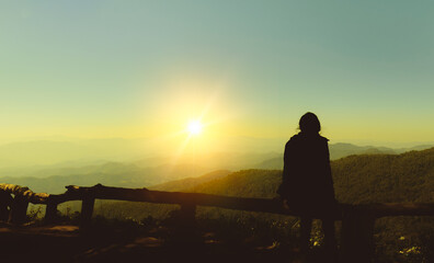Silhouette of woman sitting alone looking at watching sunset on mountain, Doi Pui ViewPoint in Chiang Mai, Thailand