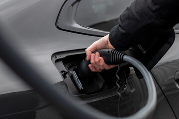 Naklejka premium Close up of electric vehicle plug in charge stop - Modern EV charging cable with man putting cable in the car - selective focus vehicle image