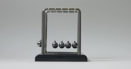 Close-up of driving a simple Newton's cradle. Kinetic pendulum. Chromatic metal balls wobble and slow down. Moving something, inertia concept, science, physics lesson. Psychological hypnosis session