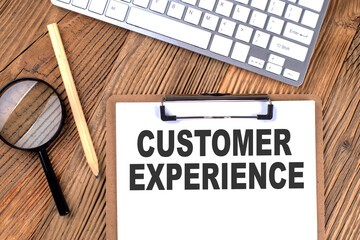 CUSTOMER EXPERIENCE text on paper clipboard with magnifier and keyboard on wooden background