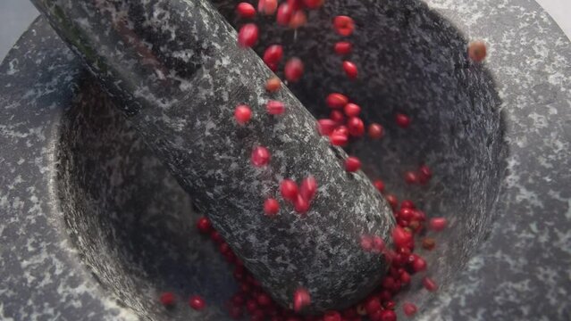 Super close-up of spicy rose peppercorns falling into the grey stone mortar