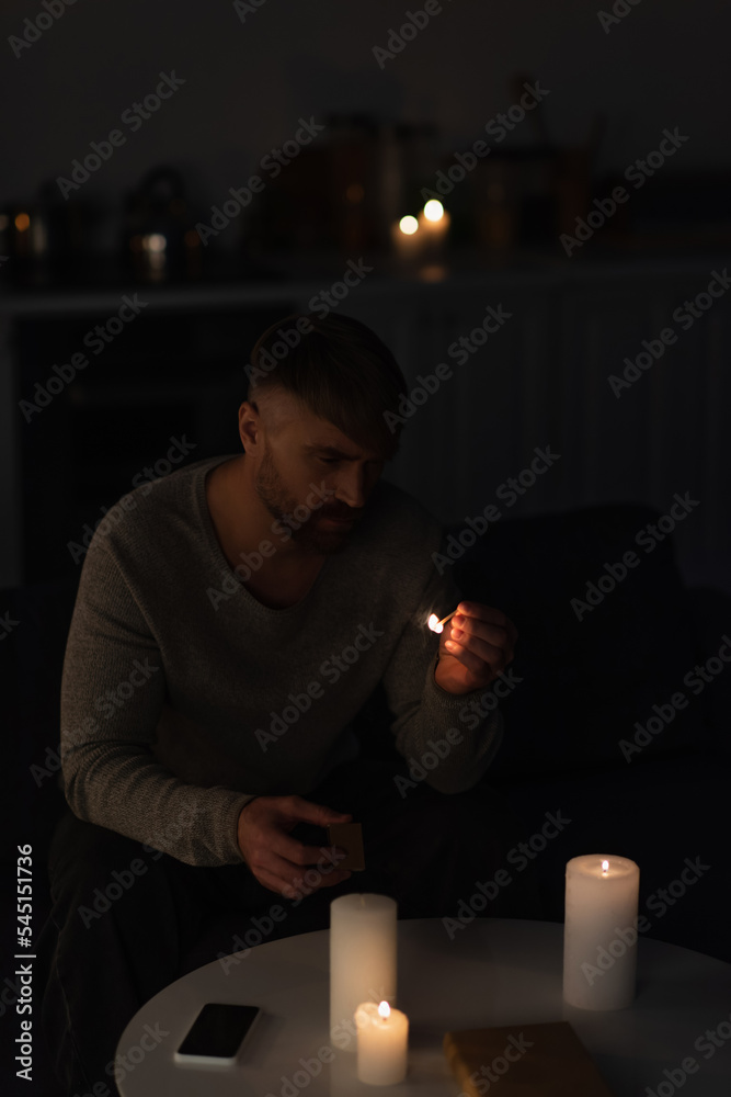 Wall mural man looking at lit match while sitting in dark kitchen near burning candles during power shutdown.