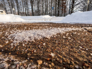 Salt grains on icy sidewalk surface in the winter. Applying salt to keep roads clear and people safe in winter weather from ice or snow. Macro view of salt grains with winter scenery in bacground