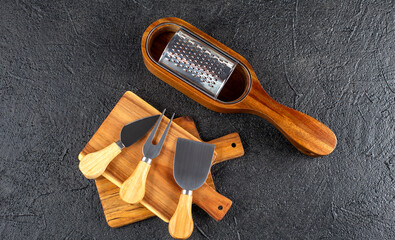 Cheese knives and cheese grater on wooden cutting board on black background , flat lay