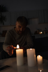 man sitting in dark kitchen during power outage and lighting candles.