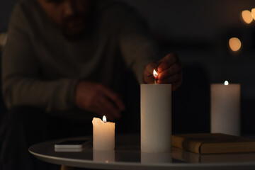 partial view of man in darkness lighting candle near book and smartphone on table.