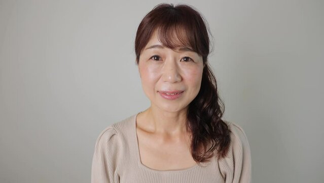 Middle aged asian woman smiles at photo studio. White wall. 25P. Dolly in.