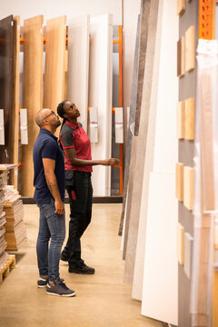 Customer and sales staff looking up while selecting laminated boards at hardware store