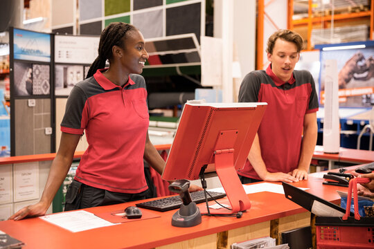 Smiling female cashier with male colleague standing at checkout in hardware store