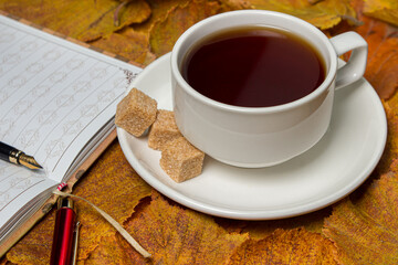 A cup of tea and a notebook on autumn leaves. Autumn tea.