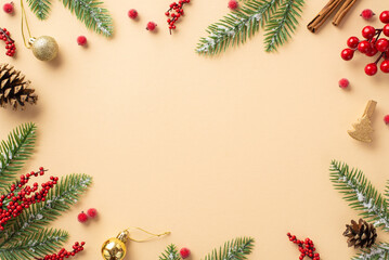 Naklejka na ściany i meble Christmas decorations concept. Top view photo of golden baubles fir branches in hoarfrost pine cones cinnamon sticks and mistletoe berries on isolated beige background with empty space in the middle