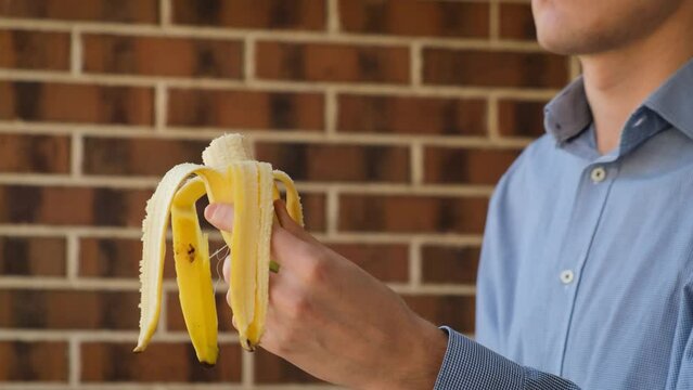 A man breaks a banana in half against the background of a wall, close-up