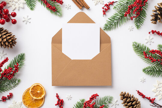 Top view photo of open craft paper envelope with letter fir branches mistletoe berries pine cones cinnamon sticks dried orange slices snowflakes on isolated white background with copyspace