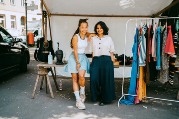 Female partners standing against table by merchandise in stall at flea market