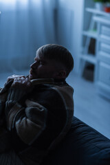 frozen man with closed eyes sitting at home under warm blanket during electricity blackout.