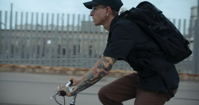 Side shot of young cool millennial man ride his single speed bike in the city on way to work or school. Hipster man commute on bicycle, ride his bike on bikelane