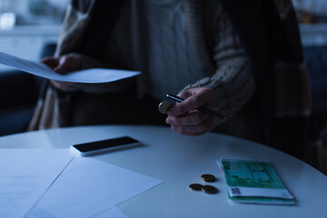 cropped view of man holding coin and payment bill near euro banknotes and cellphone during energy...