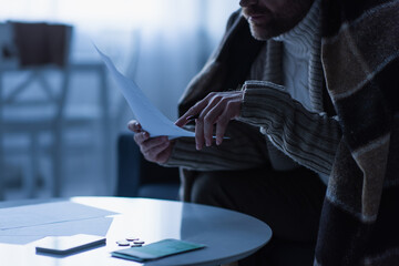 partial view of frozen man holding payment bills near money and smartphone in twilight.