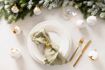 Beautiful Christmas festive table setting with white plate, champagne glasses, golden balls and napkin ring as deer on white background. Xmas festive dinner. Top view.