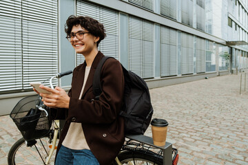 Young woman using cellphone while standing with bicycle on city street