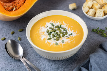 Traditional pumpkin cream soup with pumpkin seeds, thyme and croutons on a dark gray background.