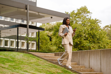 Young black businesswoman using cellphone while walking outdoors