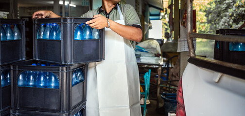 Workers lift gallons of blue drinking water and bottles in crates into the back of a transport truck.