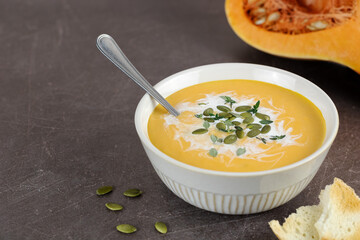 Pumpkin soup with a creamy silky texture, pumpkin seeds, fresh thyme and croutons on a brown background.