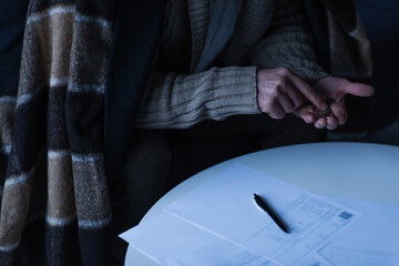 partial view of man in blanket counting coins near payment bills and pen on table.