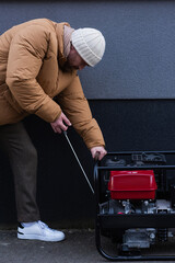 side view of man in down jacket and knitted hat starting electricity generator outdoors.