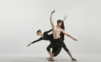 Fototapeta na wymiar Young man and woman, ballet dancers performing isolated over grey studio background. Flexibility and tenderness