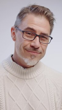 Portrait of happy casual older man looking at camera, smiling, wearing white pullover on cold winter day. Mid adult, mature age caucasian man in glasses on white background.