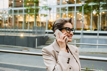 Obraz premium Mature grey woman talking on cellphone while standing on city street