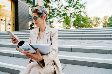 Mature woman using cellphone and working with papers outdoors