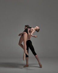 Young man and woman, ballet dancers performing isolated over dark grey studio background. Tender...