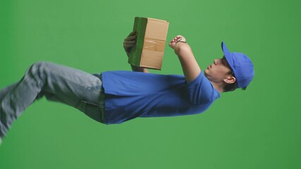 Side View Of Asian Male Courier In Blue Uniform Checking Watch And Running While Delivering A Carton On Green Screen Background In The Studio
