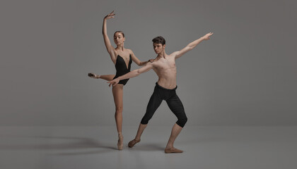 Young man and woman, ballet dancers performing isolated over dark grey studio background. Artistic...