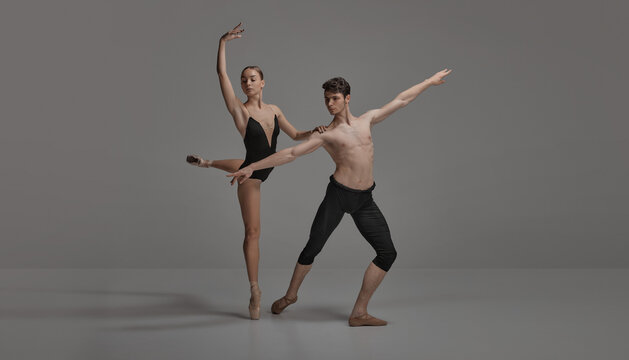 Young man and woman, ballet dancers performing isolated over dark grey studio background. Artistic movements