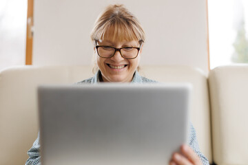 Active mature woman using a laptop for remote work from the home office. Video conference, video meeting. Senior teacher leads webinar